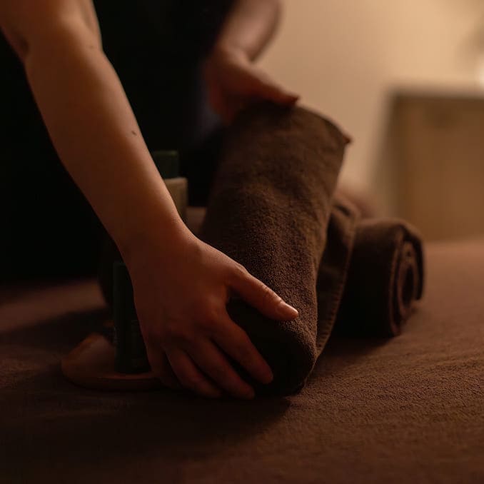 Zwinięte ręczniki spa obok butelek z olejkami, przygotowane na stół zabiegowy.