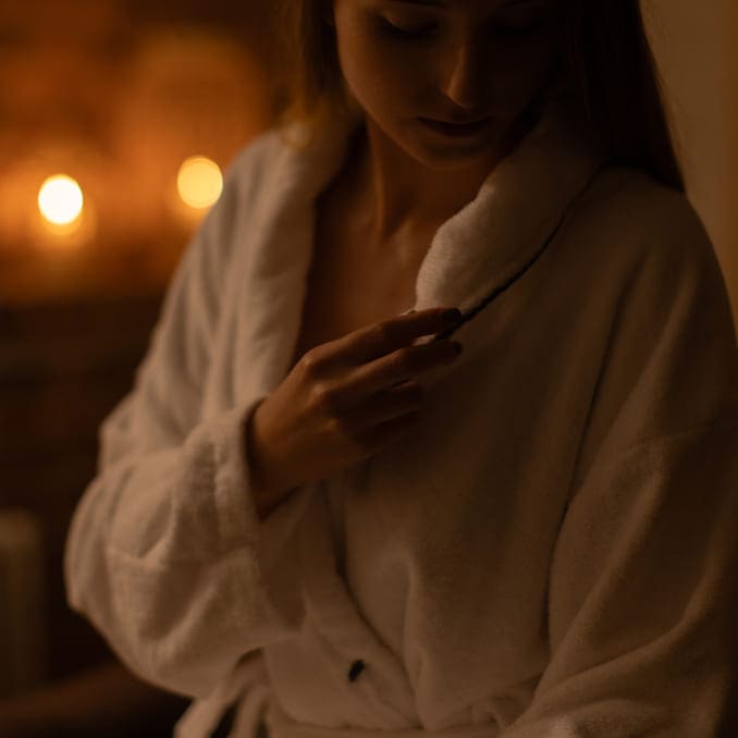 Kobieta w szlafroku siedząca w saunie, zamyślona i zrelaksowana, z zamkniętymi oczami.